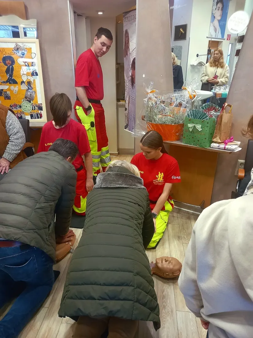 Mitglieder der DLRG/Wasserwacht in roter Uniform demonstrieren eine Herz-Lungen-Wiederbelebung an einer Übungspuppe beim Jubiläum von Haar Gefühl
